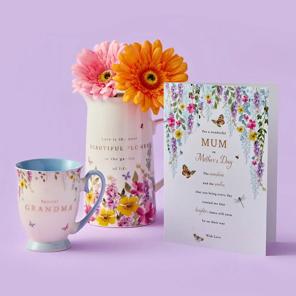 A colourful Mother’s Day set featuring a floral MUM card, a tulip‑patterned mug with matching coaster, a tall floral tumbler, and a single red tulip arranged on a pastel purple background.